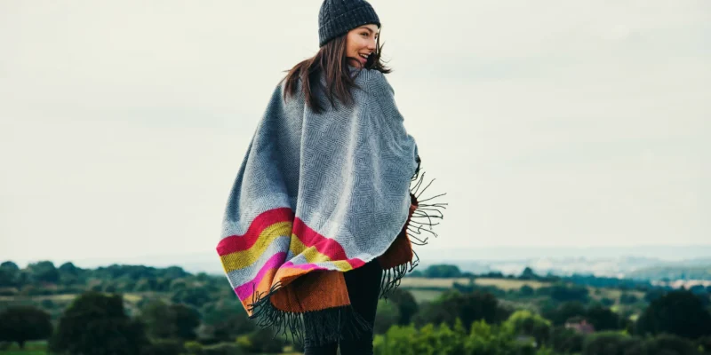 Femme en poncho stylé dans la nature automnale, entourée de collines verdoyantes.