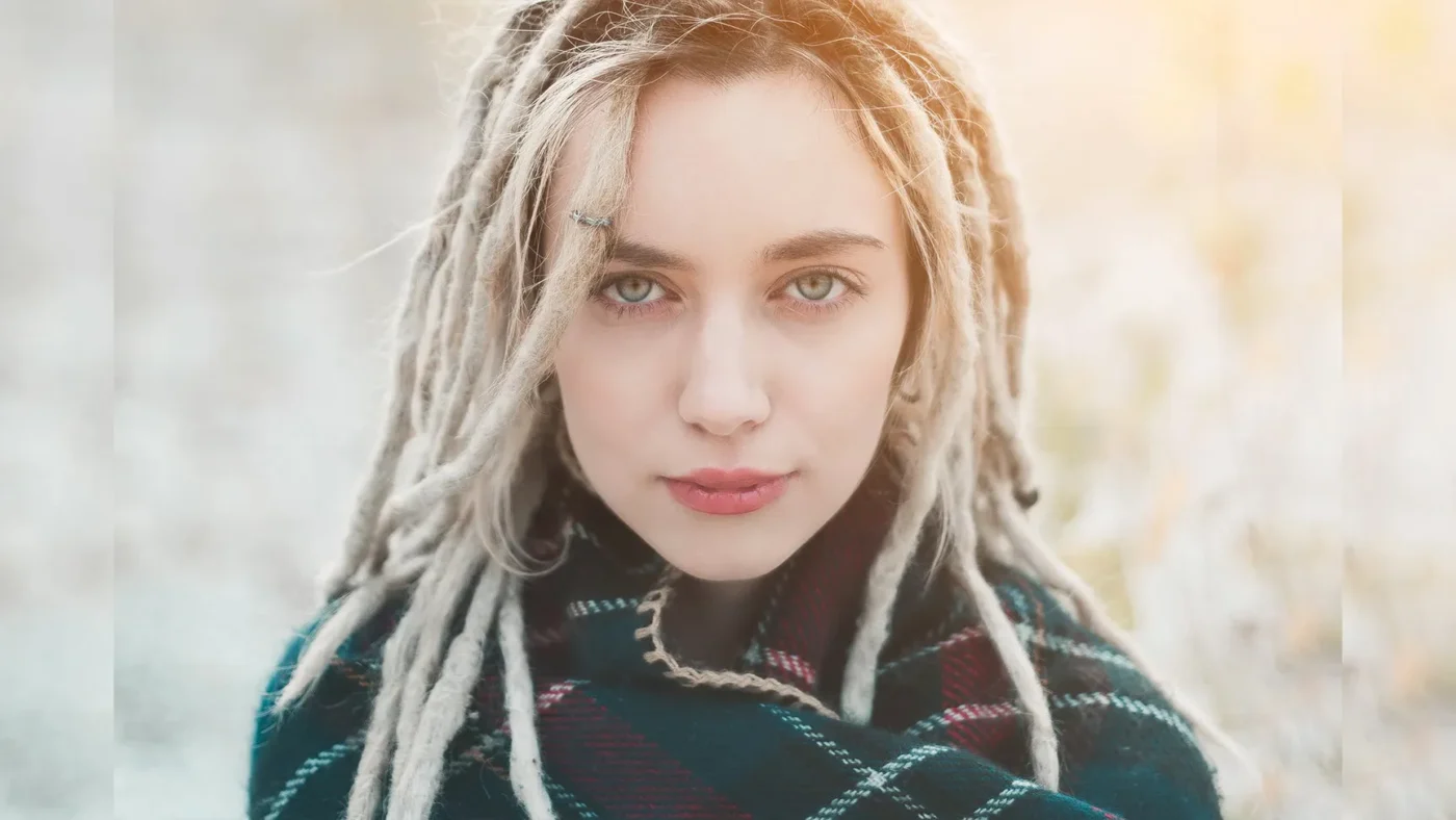 Femme élégante avec dreadlocks, poncho à carreaux, ambiance naturelle, calme et singularité.