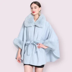 Modèle en manteau cape femme bleu clair élégant avec col en fourrure et jupe noire.