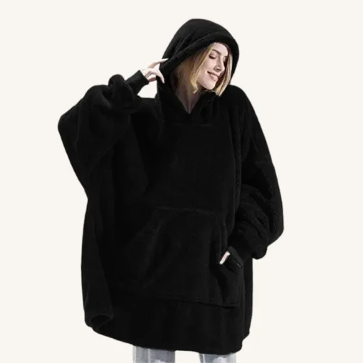 Femme souriante en poncho noir oversize, chic et confortable, avec un pantalon clair.