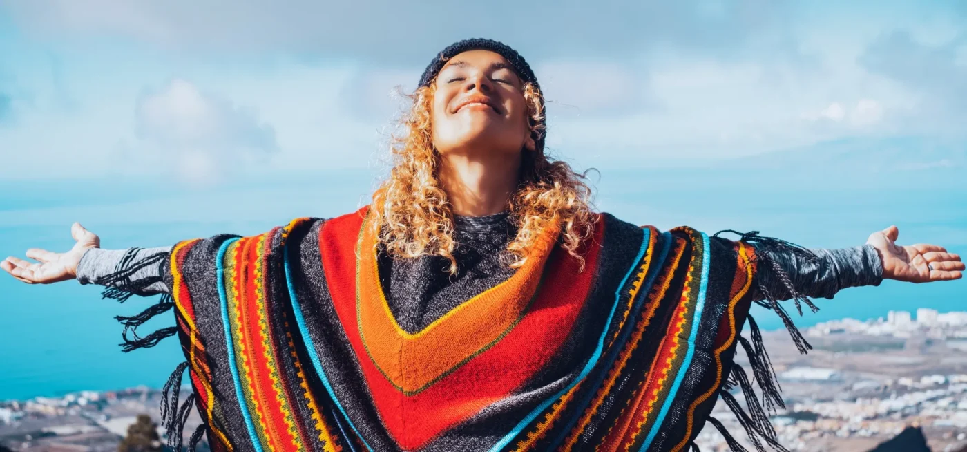 Personne joyeuse en poncho coloré face à locéan et au ciel ensoleillé.