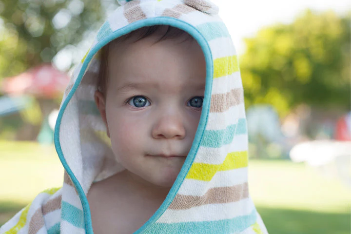 Enfant mignon dans poncho rayé, regardant la caméra, fond extérieur flou.